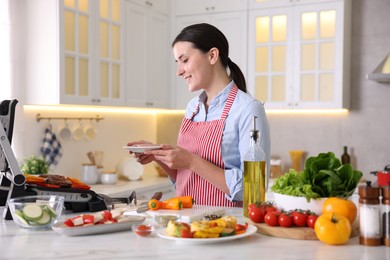 Photo of Woman cooking vegetables and meat on electric grill in kitchen