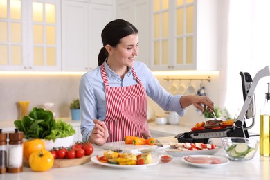 Photo of Woman cooking vegetables and meat on electric grill in kitchen