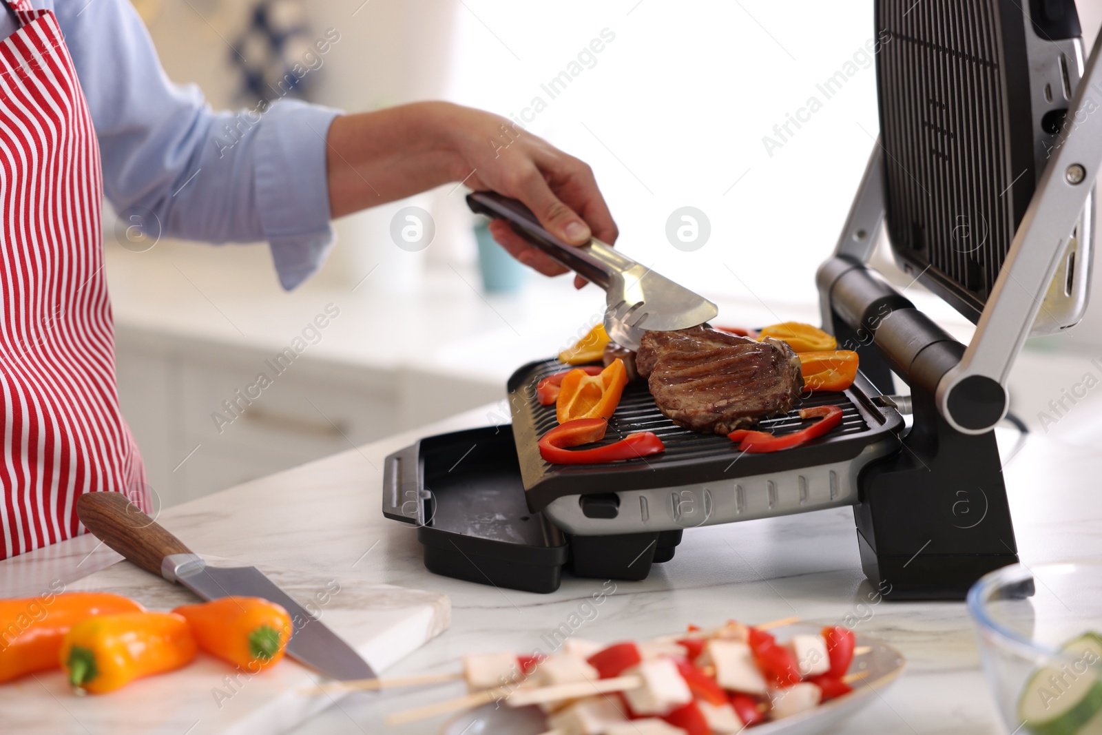 Photo of Woman cooking vegetables and meat on electric grill in kitchen, closeup