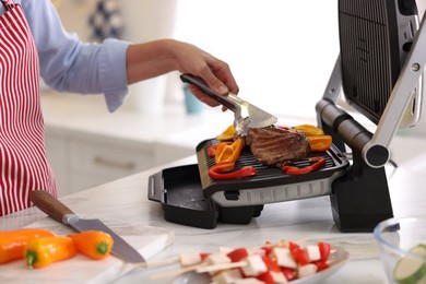 Photo of Woman cooking vegetables and meat on electric grill in kitchen, closeup