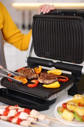 Photo of Woman cooking vegetables and meat on electric grill in kitchen, closeup