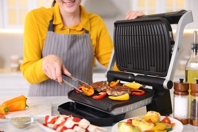 Photo of Woman cooking vegetables and meat on electric grill in kitchen, closeup