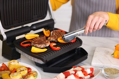 Photo of Woman cooking vegetables and meat on electric grill in kitchen, closeup