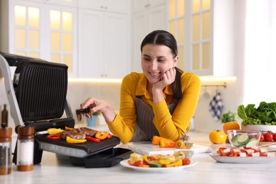 Photo of Woman cooking vegetables and meat on electric grill in kitchen