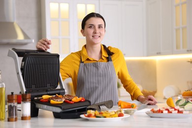 Photo of Woman cooking vegetables and meat on electric grill in kitchen