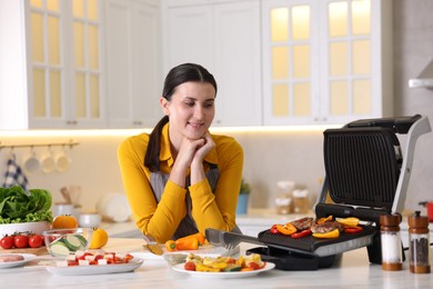 Photo of Woman cooking vegetables and meat on electric grill in kitchen