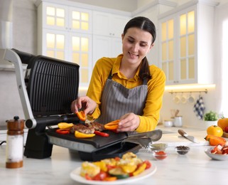 Photo of Woman cooking vegetables and meat on electric grill in kitchen
