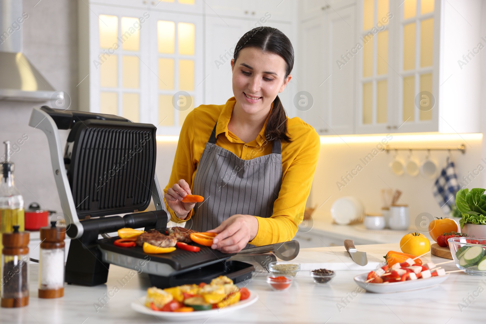 Photo of Woman cooking vegetables and meat on electric grill in kitchen