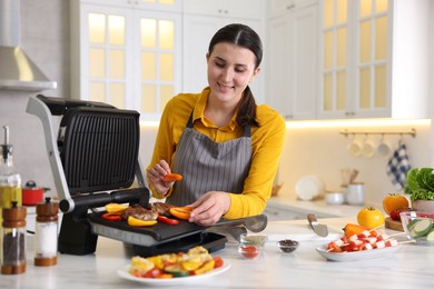 Photo of Woman cooking vegetables and meat on electric grill in kitchen