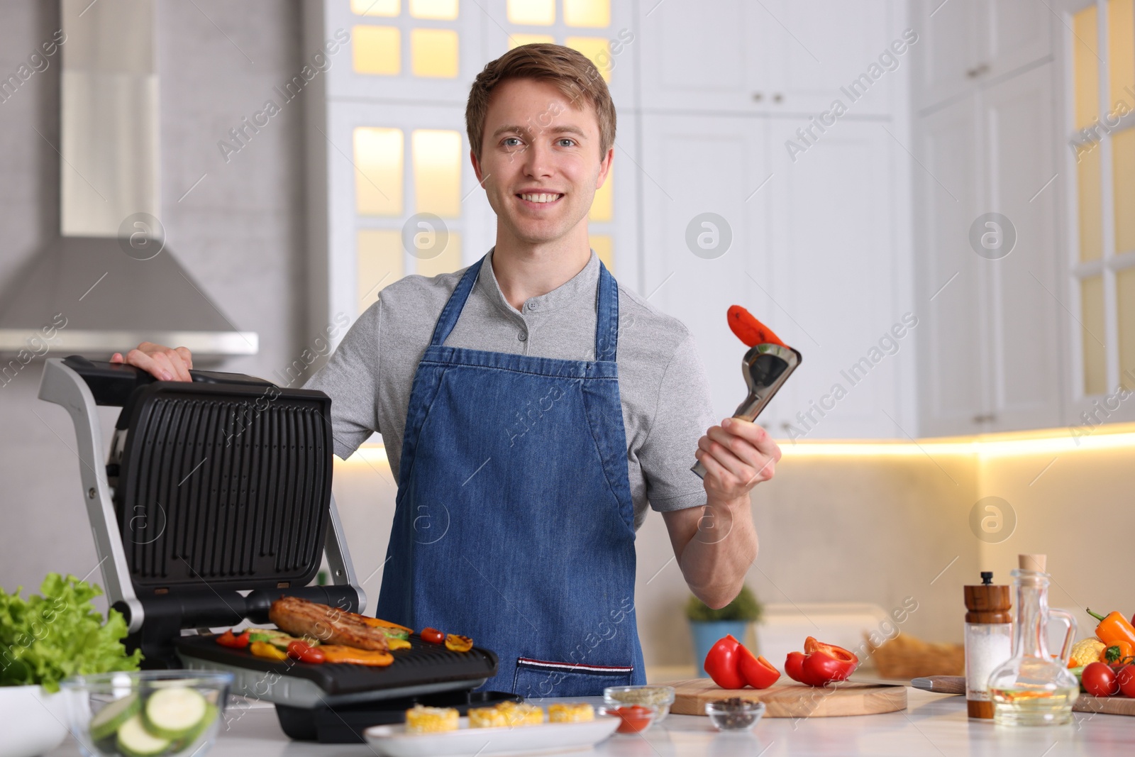 Photo of Man cooking vegetables and meat on electric grill in kitchen