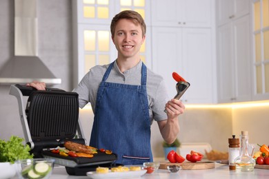 Photo of Man cooking vegetables and meat on electric grill in kitchen
