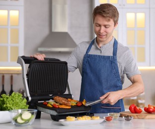 Photo of Man cooking vegetables and meat on electric grill in kitchen