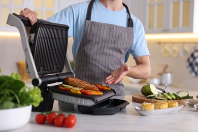 Photo of Man cooking vegetables and meat on electric grill in kitchen, closeup