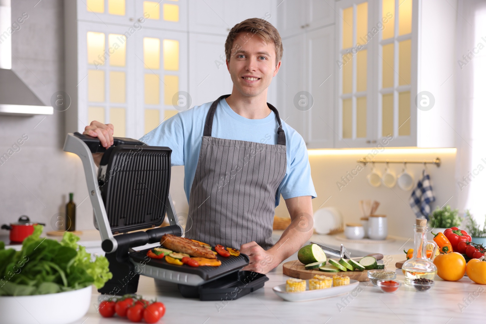 Photo of Man cooking vegetables and meat on electric grill in kitchen
