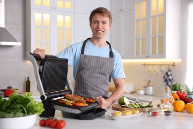 Photo of Man cooking vegetables and meat on electric grill in kitchen