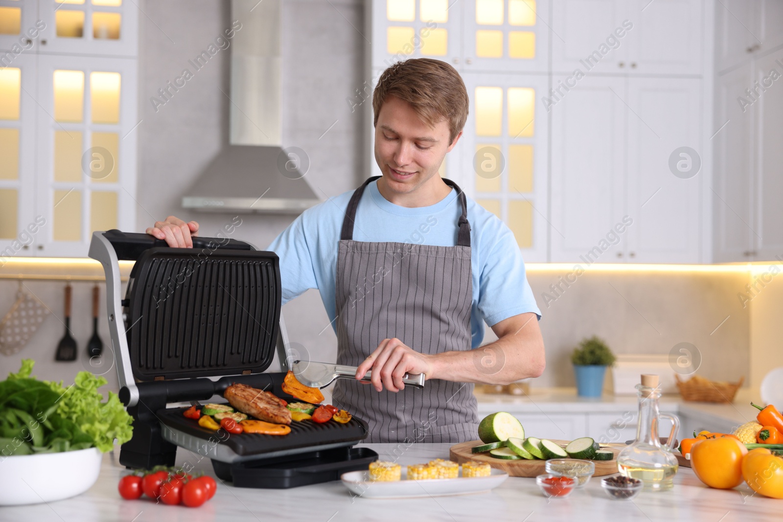 Photo of Man cooking vegetables and meat on electric grill in kitchen