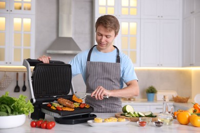 Photo of Man cooking vegetables and meat on electric grill in kitchen