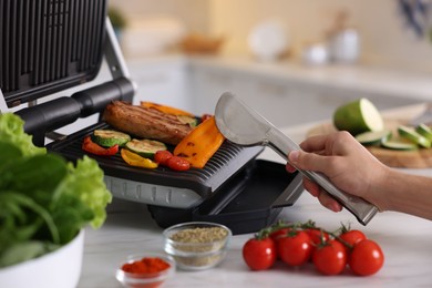Photo of Man cooking vegetables and meat on electric grill in kitchen, closeup