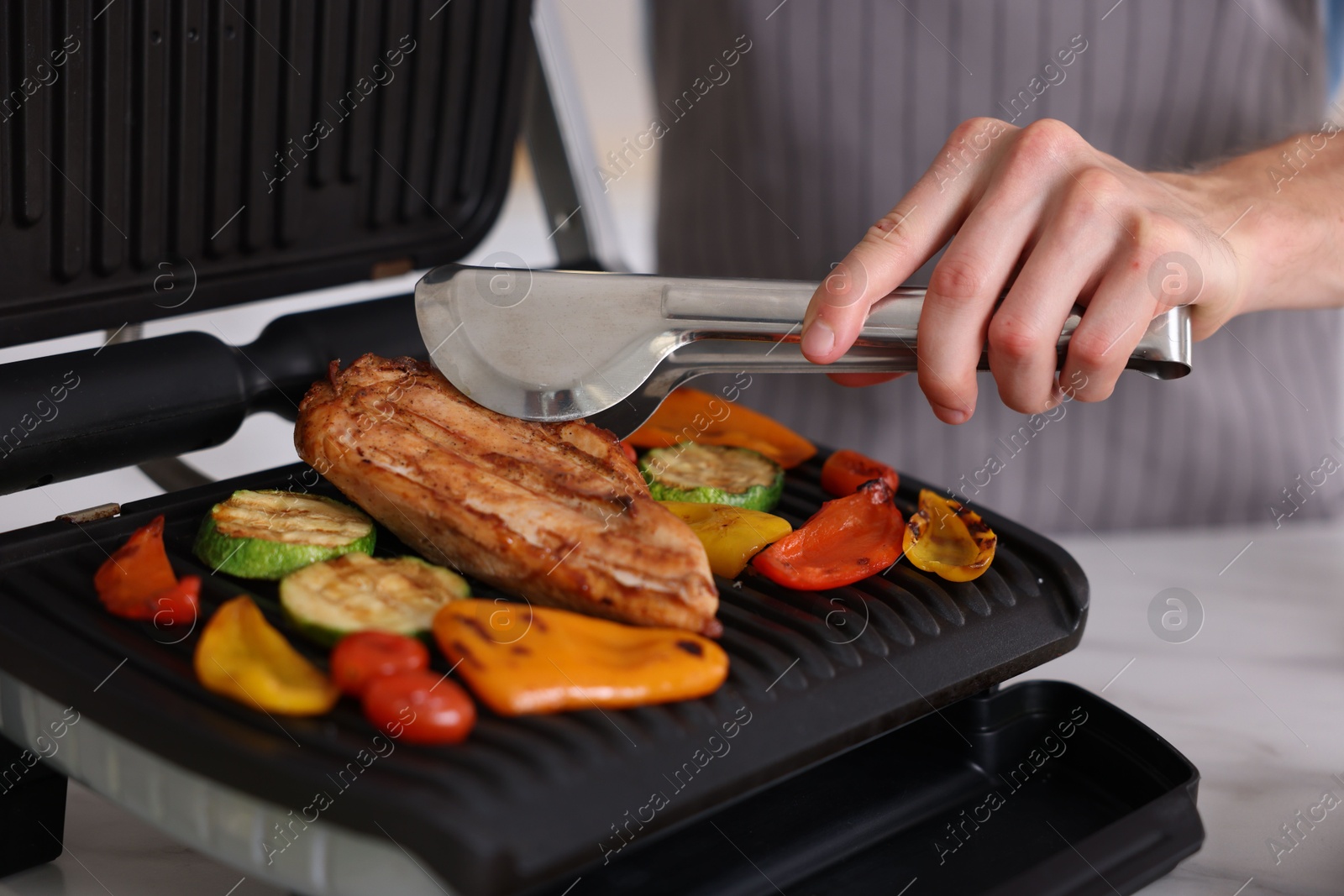Photo of Man cooking vegetables and meat on electric grill in kitchen, closeup