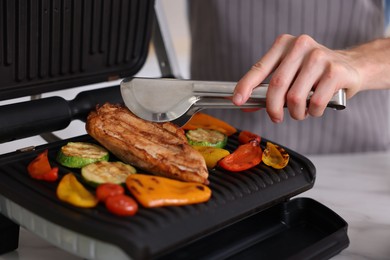 Photo of Man cooking vegetables and meat on electric grill in kitchen, closeup