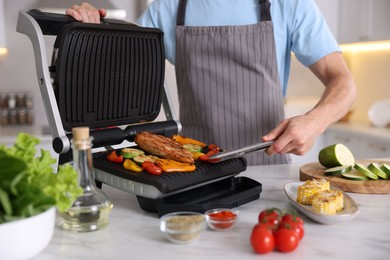 Photo of Man cooking vegetables and meat on electric grill in kitchen, closeup