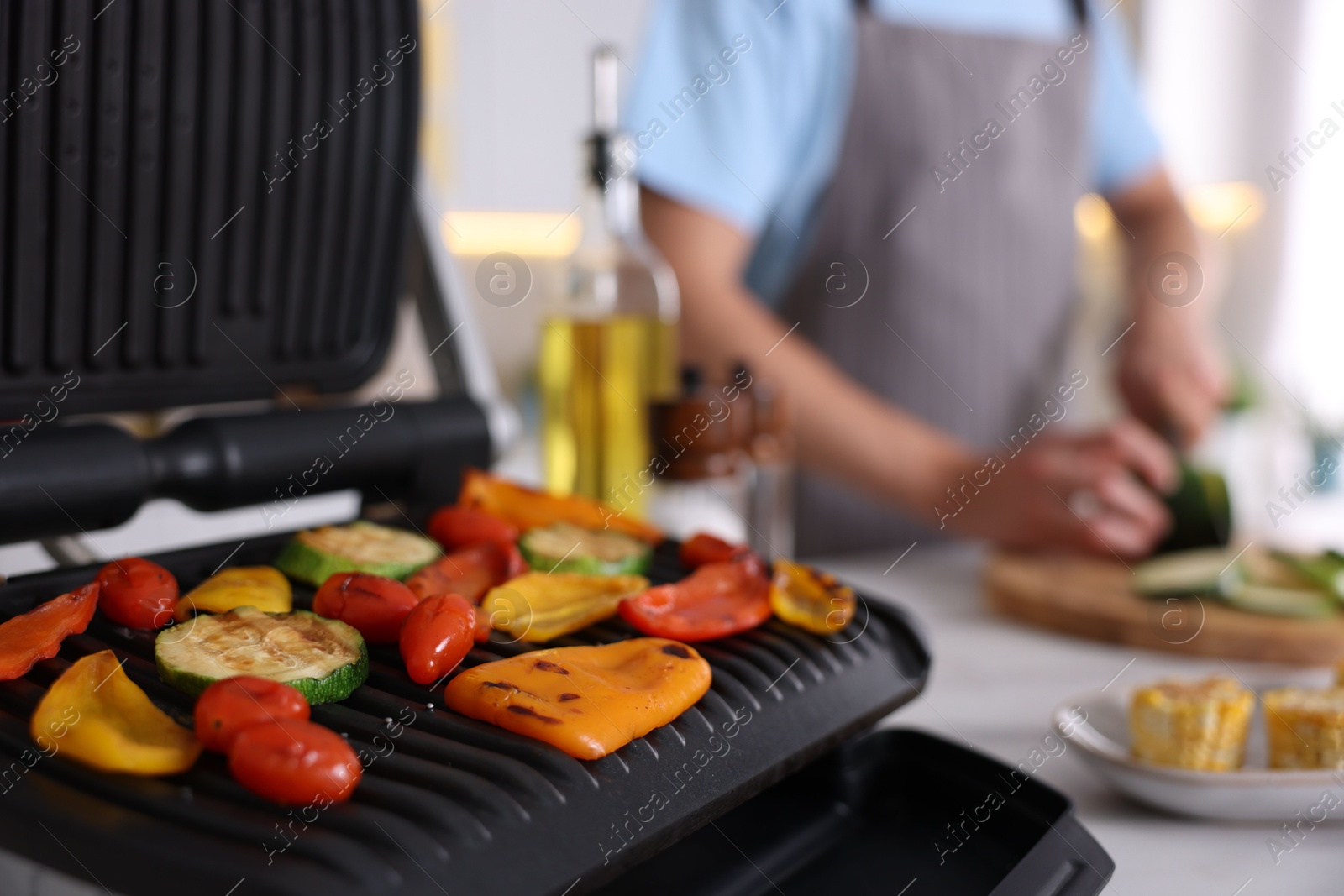 Photo of Man cutting zucchini while cooking vegetables on electric grill in kitchen, closeup