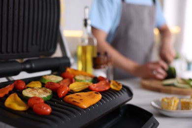 Photo of Man cutting zucchini while cooking vegetables on electric grill in kitchen, closeup