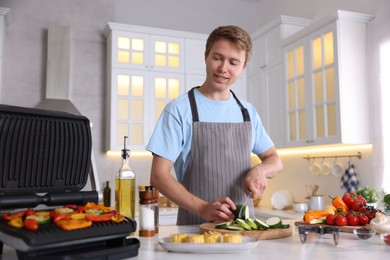 Photo of Man cutting zucchini while cooking vegetables on electric grill in kitchen