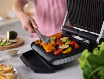 Photo of Man cooking vegetables on electric grill in kitchen, closeup