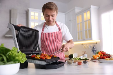Photo of Man cooking vegetables on electric grill in kitchen