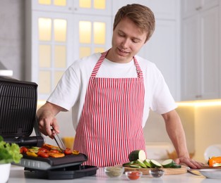 Photo of Man cooking vegetables on electric grill in kitchen