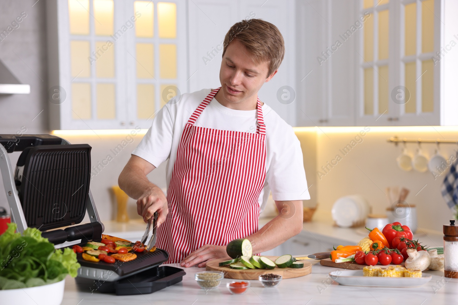 Photo of Man cooking vegetables on electric grill in kitchen
