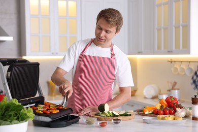 Photo of Man cooking vegetables on electric grill in kitchen