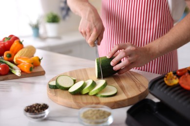Photo of Man cutting zucchini at table in kitchen, closeup