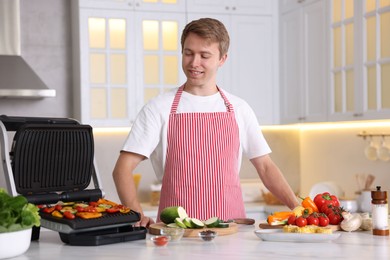 Photo of Man cooking vegetables on electric grill in kitchen