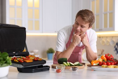 Photo of Man cooking vegetables on electric grill in kitchen