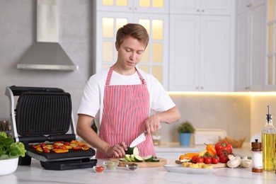 Photo of Man cutting zucchini while cooking vegetables on electric grill in kitchen