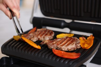Photo of Man cooking meat and vegetables on electric grill in kitchen, closeup