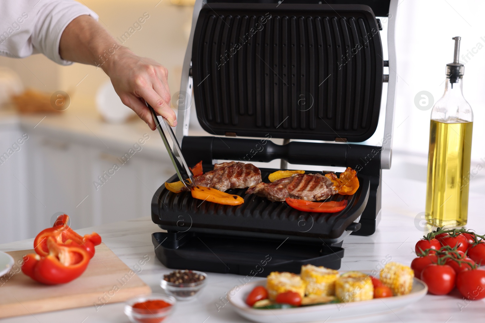 Photo of Man cooking meat and vegetables on electric grill in kitchen, closeup