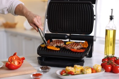 Photo of Man cooking meat and vegetables on electric grill in kitchen, closeup