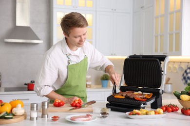 Photo of Man cooking meat and vegetables on electric grill in kitchen