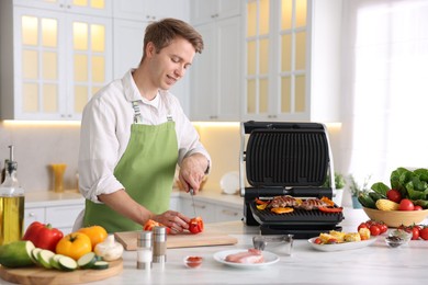 Photo of Man cutting pepper while cooking vegetables on electric grill in kitchen