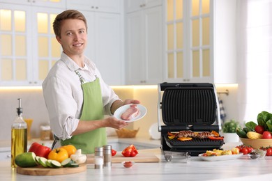 Photo of Man cooking meat and vegetables on electric grill in kitchen