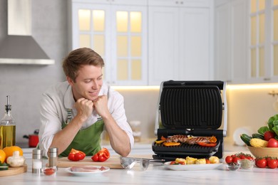 Photo of Man cooking meat and vegetables on electric grill in kitchen