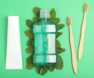 Photo of Mouthwash, other oral hygiene products and mint on green background, flat lay
