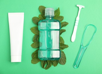 Photo of Mouthwash, other oral hygiene products and mint on green background, flat lay
