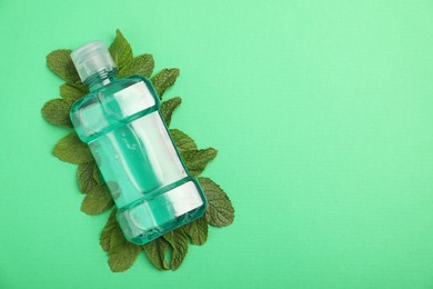 Photo of Bottle of mouthwash and mint leaves on green background, top view. Space for text