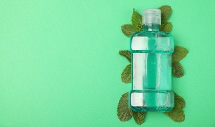 Photo of Bottle of mouthwash and mint leaves on green background, top view. Space for text