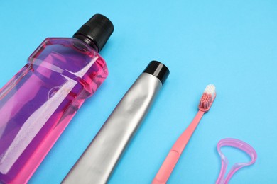 Photo of Mouthwash, toothbrush, toothpaste and tongue scraper on light blue background, closeup