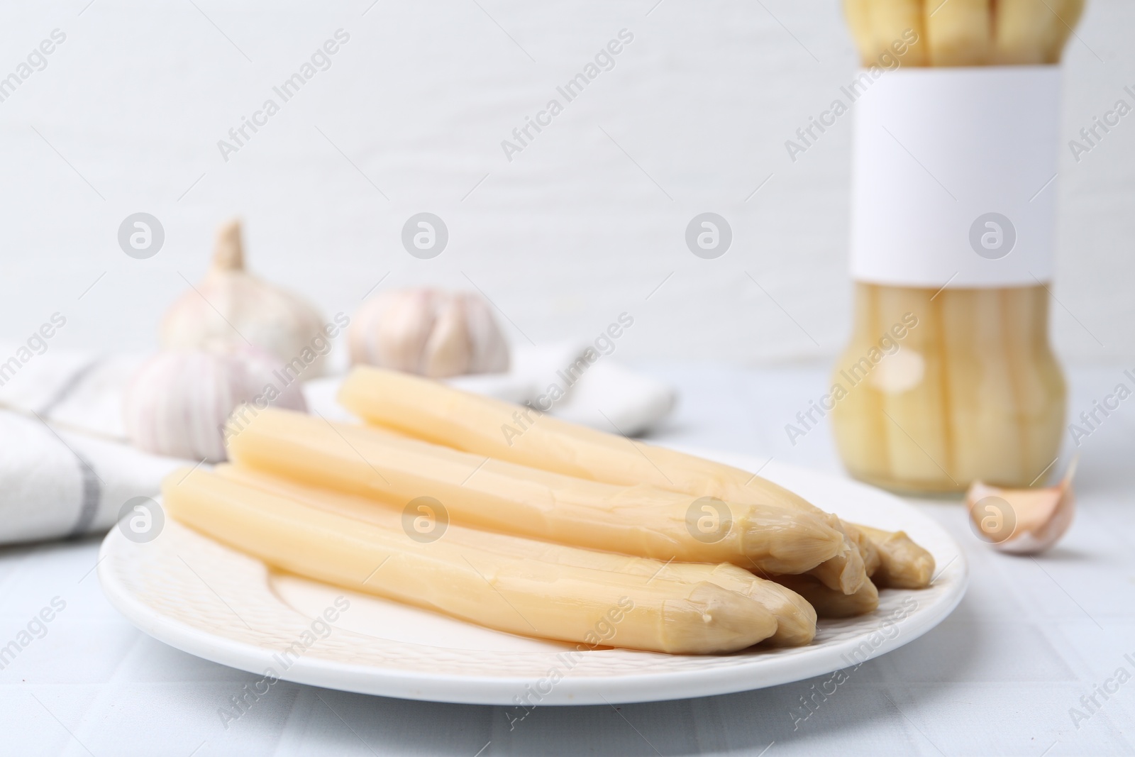 Photo of Pickled asparagus and garlic on white tiled table, closeup